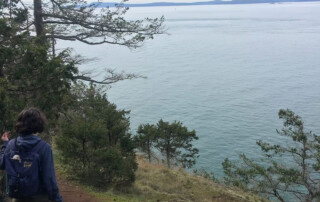 Aurora stands on a hiking trail overlooking the ocean.