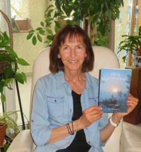 A woman. Liz Kornelsen, smiling and holding her book, Arc of Light and Shadow.