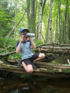 Child sitting on log, looking through magnifying glass