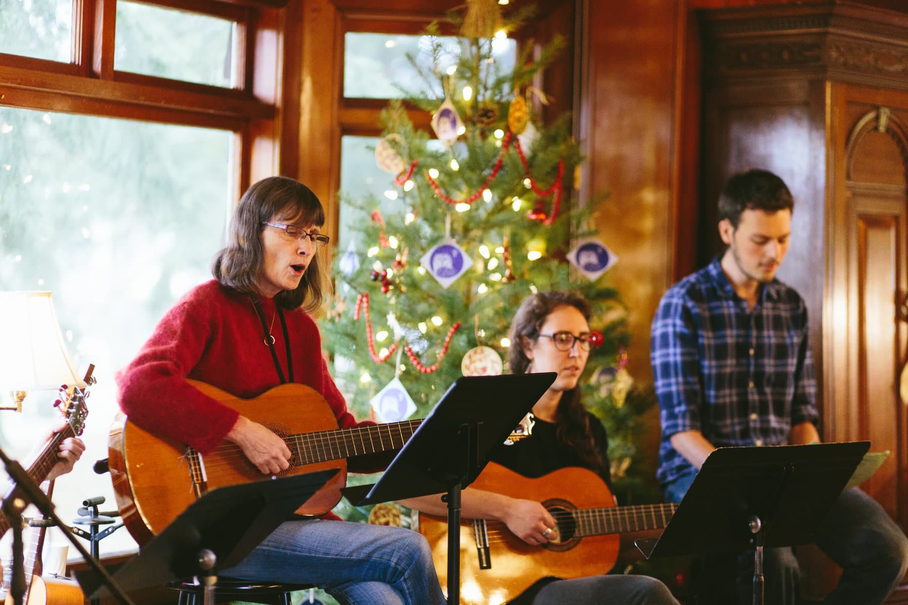 Two Women and a man singing in front of a Christmas tree