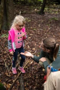Jacoba, young woman, holding out moss specimen in her hand for a young girl to examine.
