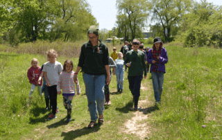Jacoba, Program Coordinator, leading a group of children on a walk in the field.