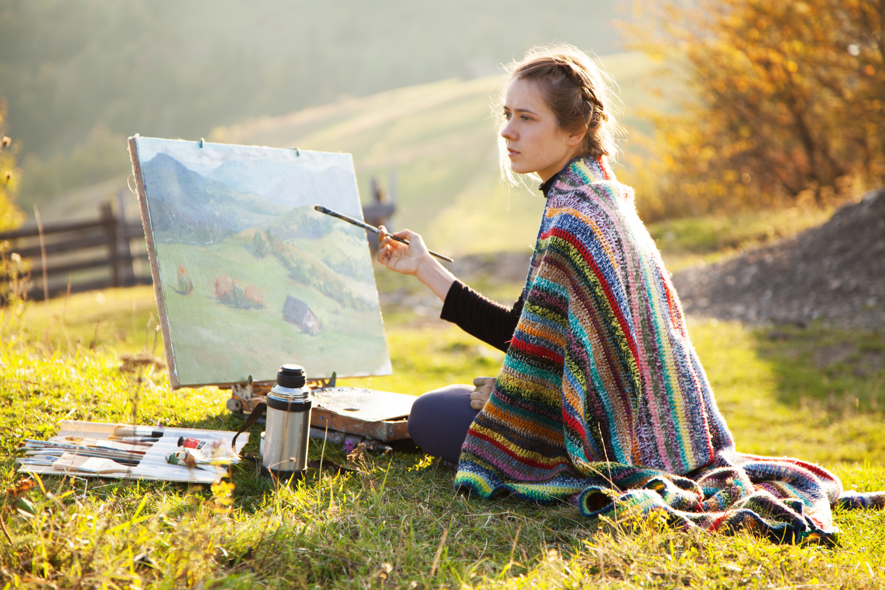 Woman sitting on the grass at Cedar Haven, painting a landscape image.