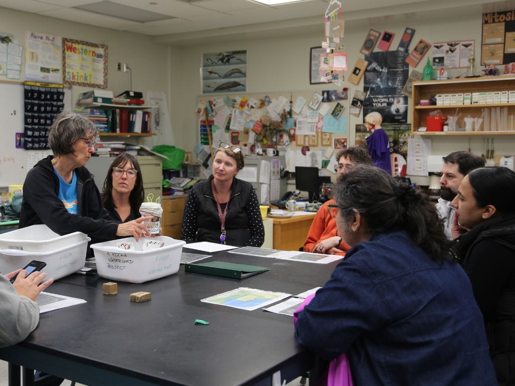 Adults seated around a table with watershed kit demonstration by a facilitator